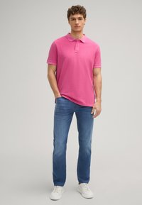 Lichtroze polo shirt met een kraag en korte mouwen, gecombineerd met lichtblauwe jeans en witte sneakers. Eenvoudig, casual ontwerp met minimale details.