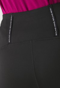 Leggings sportivi neri con una texture liscia, vita alta e etichette laterali con la scritta "SOUND MIND, SOUND BODY" stampata in bianco.