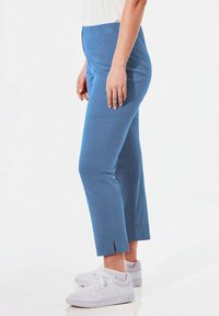 Blauwe stretch katoenen broek met een aansluitende taille en zijsplitten aan de zoom, gecombineerd met witte sneakers.