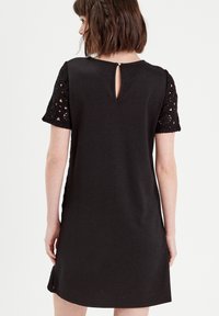 Robe noire avec des manches courtes en crochet et une ouverture en forme de goutte d'eau au dos. Fabriquée en tissu lisse, avec une coupe droite et décontractée.
