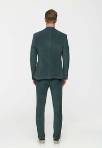 Zöld kordbársony öltöny függőleges csíkokkal, fitted zakóval és csőnadrággal. Figyelemre méltó textúra és sima felület, sportos cipővel viselve.