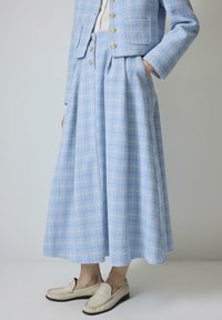 Svetle modrý kostým z tkaniny tweed s kratší bundou a sukní do délky kolen se zakládanými záhyby. Zlaté knoflíky na bundě; texturovaný vzor po celém povrchu.