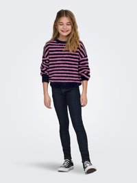 Csíkos pulóver rózsaszín és tengerészkék színekben, bolyhos textúrával, sötét szűk farmerrel és fekete sportcipővel párosítva. Egyszerű kerek nyakkivágással és hosszú ujjakkal.