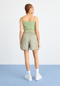 Olivovo zelený rebrovaný crop top a svetlozelené šortky s elastickým pásom, doplnené bielymi teniskami a ponožkami do pol lýtok.
