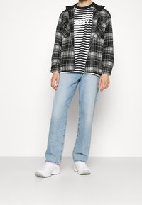 Black and white plaid jacket over a striped black and white t-shirt, paired with light blue jeans and white sneakers.