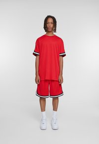 Costum sportiv roșu format dintr-un tricou lejer și pantaloni scurți cu accente în dungi negre și albe. Material din amestec de bumbac, croială relaxată și mâneci scurte.