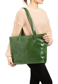 Sac fourre-tout en cuir vert avec une finition brillante, de forme plate et deux poignées robustes. Le sac n'a aucun motif visible ni détail en matériel.