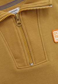 Geel ribbeltrui met halve rits, voorzien van een ritssluiting, zichtbaar merklabel en een klein label met de tekst "GOOD TIME" op de borst.