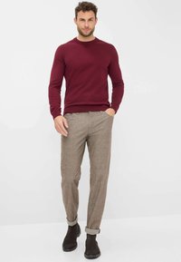 Bordeauxfarbener Rundhalsausschnitt-Pullover, beigefarbene, strukturierte Hose mit umgeschlagenen Säumen und dunkelbraunen Wildlederstiefeln. Schlichtes und modernes Design.