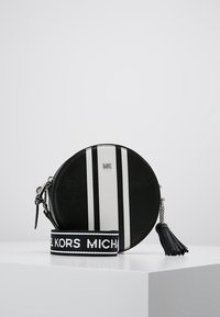 Borsa circolare in pelle nera con strisce verticali bianche, con logo "MK" in cima. Presenta una tracolla removibile e un accento a frange.