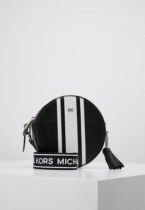 Circular black leather bag with white vertical stripes, branded "MK" on top. Features a detachable strap and a tassel accent.