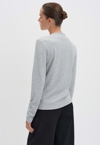 Maglietta a maniche lunghe grigia con collo rotondo e tessuto testurizzato, abbinata a pantaloni neri a gamba larga. Mostra la vista posteriore dell'outfit.