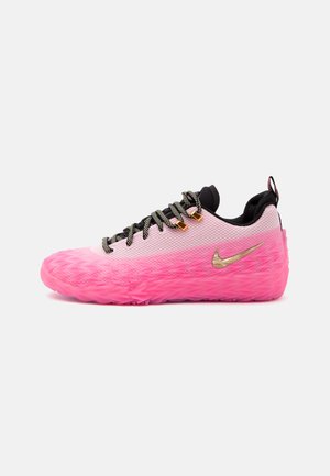 Ροζ και λευκό αθλητικό Nike χαμηλού τύπου με ανάγλυφη ροζ σόλα, χρυσό σήμα Nike, μαύρη γλώσσα και μαυρόασπρα κορδόνια σε λευκό φόντο.