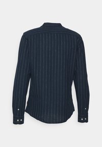 Camisa de manga larga azul marina con delgadas rayas blancas verticales, con puños abotonados, mostrada desde la parte posterior frente a un fondo blanco liso.