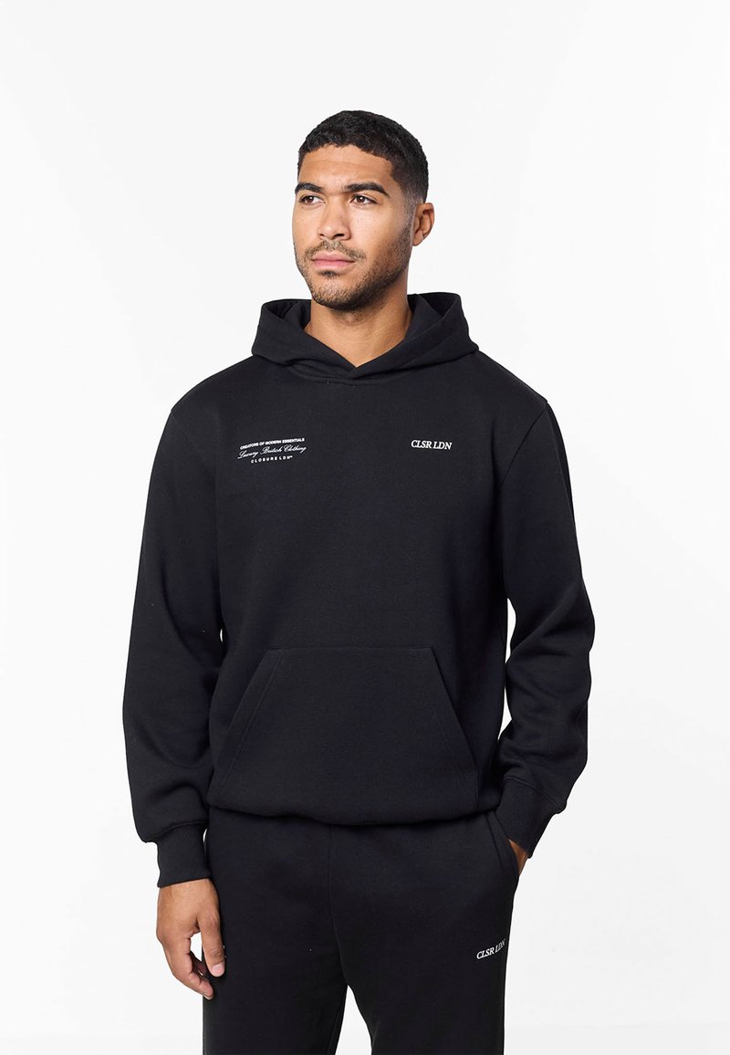 Zwarte hoodie met een voorvak, voorzien van witte tekstbranding op de borst en linkermouw. Gemaakt van zachte stof met een losse pasvorm.
