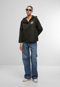 Black lightweight hooded jacket with a front logo, paired with loose blue denim jeans and off-white sneakers. Smooth fabric texture.