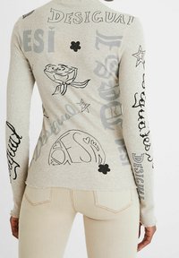 Haut à manches longues gris stock avec des imprimés graphiques noirs, incluant du texte et des motifs floraux, doté d'une texture côtelée et d'un ourlet brut.