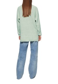 Muntgroene oversized gebreide trui met een gestructureerde afwerking, gecombineerd met lichtblauwe brede spijkerbroek. De outfit heeft een ontspannen vorm en silhouet.