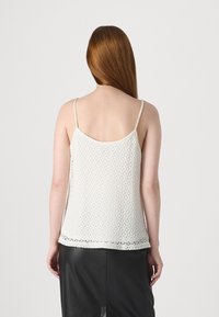 Hvit heklet tanktopp med tynne stropper, med et åpent blondermønster og bølget kant, kombinert med et svart skjørt.