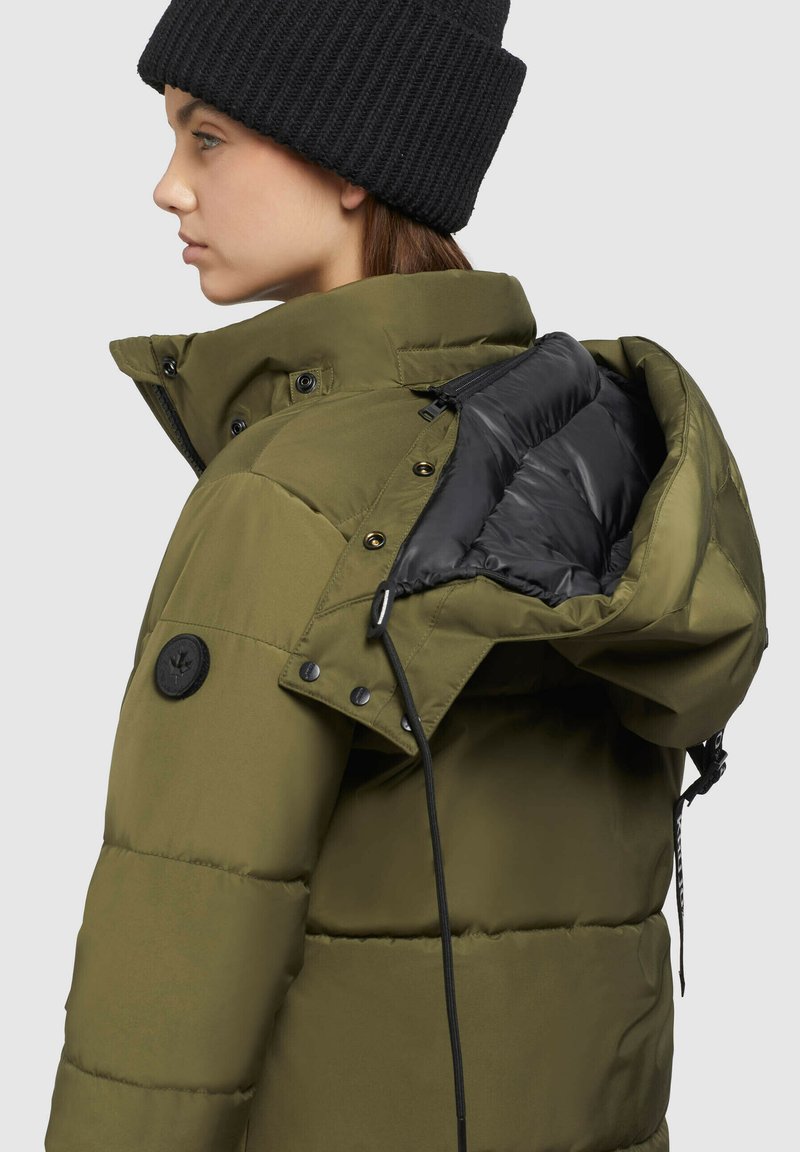 Olivgrüne Pufferjacke mit schwarzer Innenauskleidung, großen Knöpfen und verstellbarem Zugband an der Kapuze, ausgestattet mit einer Reißverschlusstasche.