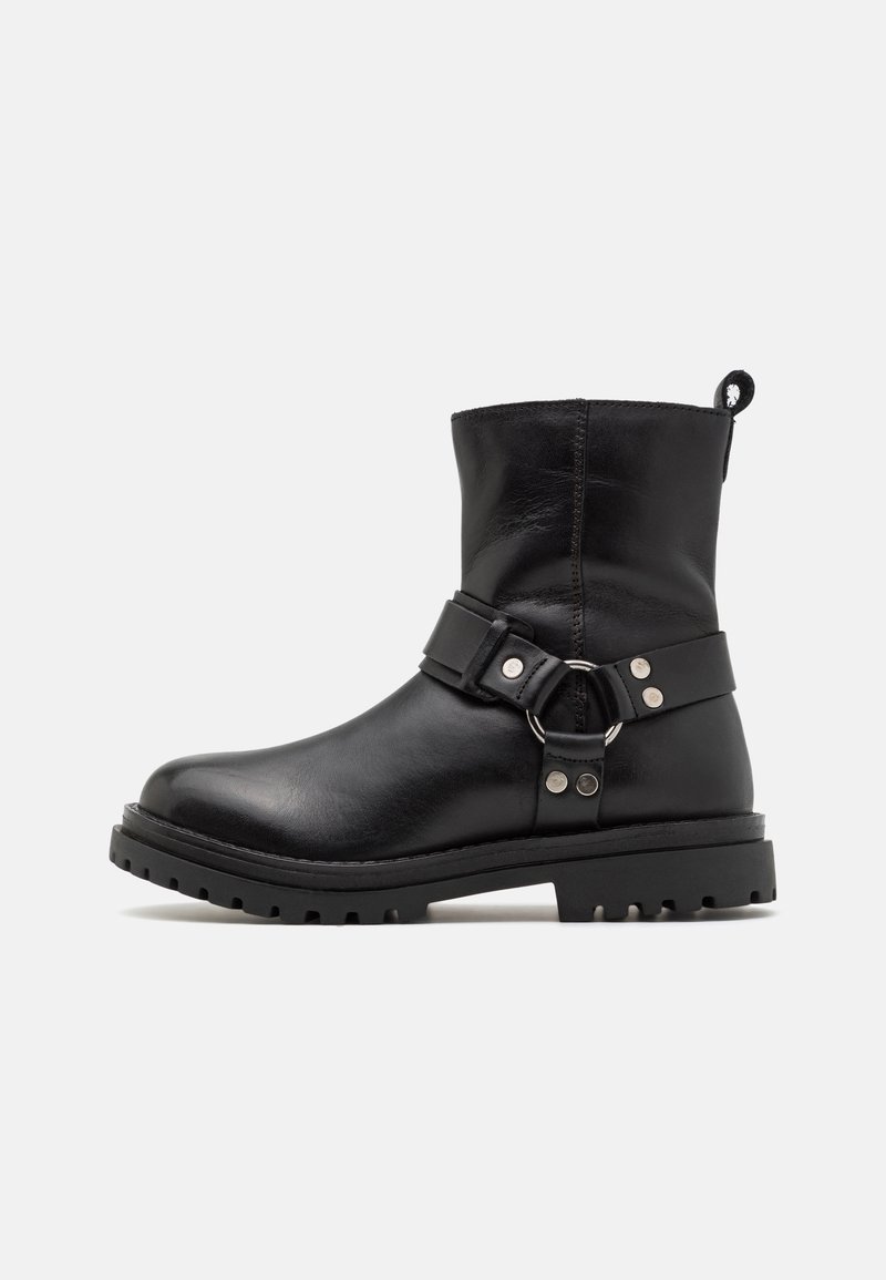 Bottine en cuir noir avec bout rond, semelle robuste, et sangle décorative avec anneau métallique et rivets sur le côté.