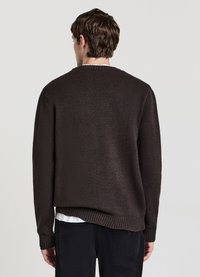 Brauner Strickpullover mit Rundhalsausschnitt und gerippten Bündchen, mit lockerem Sitz und strukturierter Oberfläche, getragen über einem weißen Hemd.