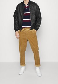 Černá kožená bomber bunda přes námořnickou a vínovou pruhovanou polo tričko, doplněná béžovými kordovými kalhotami a bílými teniskami.