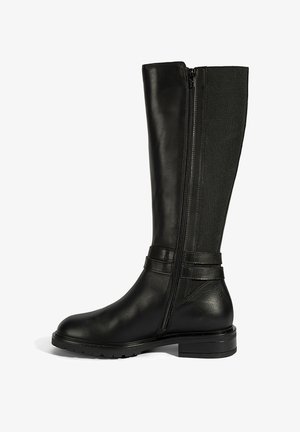 Botte noire montante en cuir brillant avec un panneau en tissu flexible. Présente une fermeture éclair sur le côté et deux sangles décoratives horizontales.