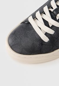 Μαύρο αθλητικό παπούτσι με υφή, λευκά κορδόνια, στρογγυλερή μύτη και αντίθετη ανοιχτόχρωμη σόλα. Διαθέτει ορατή ραφή κ ατά μήκος της άκρης.