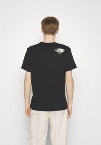 Černé bavlněné tričko s krátkým rukávem, které na horní části zad má bílo-zelené logo. Jednoduchý, uvolněný střih.