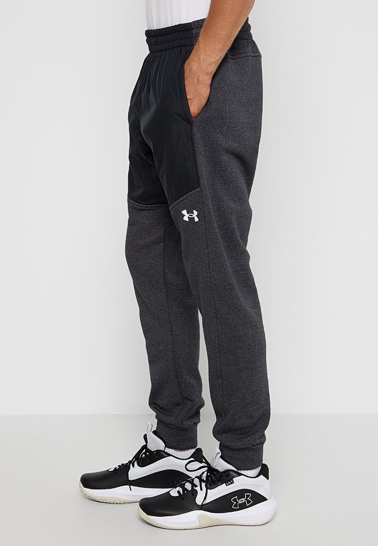 Pantalones deportivos en felpa gris oscuro con un panel negro en el lateral, que cuentan con una cinturilla elástica y un logo blanco en la pierna.