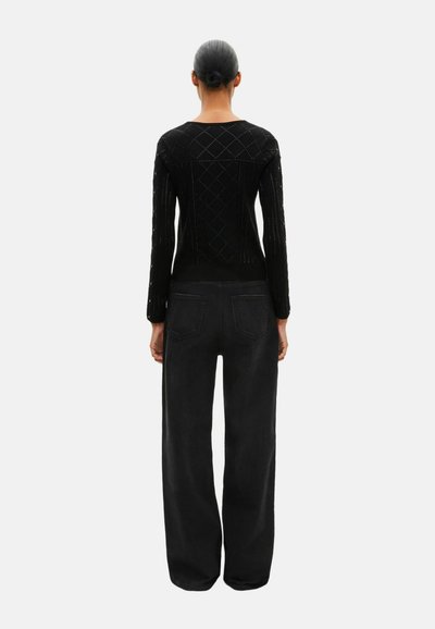 Czarny sweter dziergany z wzorem diamentu na plecach, w połączeniu z czarnymi jeansami z wysokim stanem i tylnymi kieszeniami.