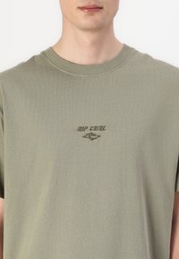 Olive green cotton t-shirt with a classic crew neckline. Features a textured, embroidered "RIP CURL" logo on the chest.