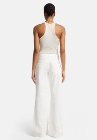 Witte wijde broek van lichtgewicht stof, gecombineerd met een beige geribbelde tanktop. Heeft een getailleerde bodice en zichtbare stikseldetails.