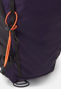 Purple backpack made of durable fabric. Features black straps, an orange accent cord, and a clip for securing additional items.