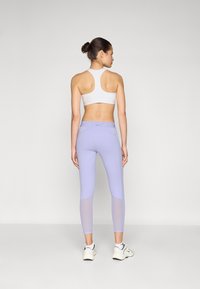 Lyse lilla leggings med netdetaljer og en hvid sportsbh, der har en tætsiddende pasform til aktivt tøj. Vist fra bagvægten.