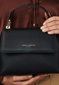 Zwarte leren handtas met een gestructureerde afwerking, goudkleurige hardware, een omslagflap en een kort handvat. Merknaam: Isabel Bernard, Parijs.