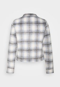 Veste à manches longues à carreaux gris, blanc et bleu clair vue de dos sur un fond clair uni.