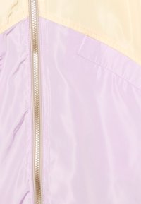 Ljuslila och krämfärgad färgblockjacka med en central silvrig dragkedja och en liten rektangulär sydd ficka på höger sida.