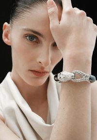 Pulsera de diseño de serpiente plateada con una banda negra brillante, que presenta texturas y eslabones intrincados, llevada en una muñeca humana sobre un fondo oscuro.