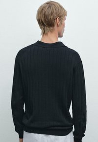 Zwarte geribbelde breiselsweater met een kraaghalslijn en lange mouwen. Heeft een textuurpatroon en een ontspannen pasvorm.