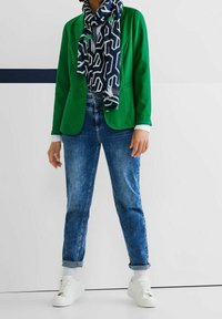 Zielona marynarka, wzorzysty niebieski szalik, jasnoniebieska koszula, wyblakłe niebieskie dżinsy i białe trampki. Gładkie tekstury z podwiniętymi mankietami.