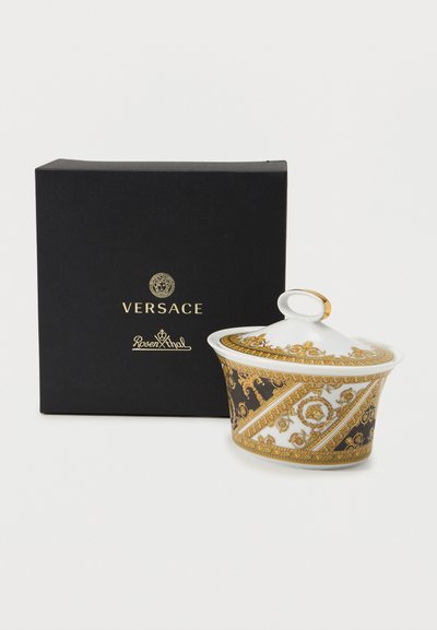 Πορσελάνινο δοχείο με χρυσαφένιο και μαύρο διακοσμητικό μοτίβο Versace, λευκό καπάκι με χρυσή λεπτομέρεια, δίπλα σε μαύρο κουτί με το λογότυπο Versace Rosenthal.