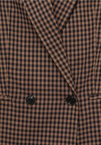 Blazer croisé marron et noir à carreaux avec deux boutons noirs et revers crantés.