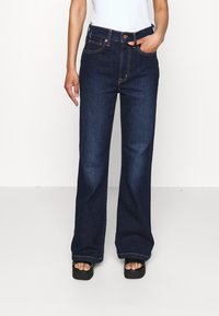 Bredde ben mørk denim jeans med høy liv, med oransje sømmer og frontlommer. Kombinert med svarte plattform sandaler.