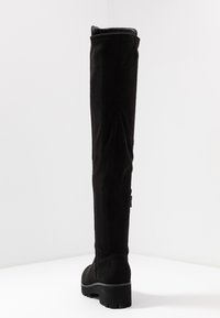 Stivale nero al ginocchio realizzato in suede con una texture liscia, gambale largo, suola in gomma spessa e tacco leggermente rialzato per maggiore altezza.