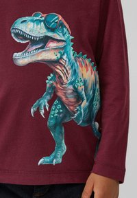 Bordeauxfarbenes Langarmshirt mit einem bunten T-Rex-Graphic, der Sonnenbrillen trägt. Der Dinosaurier hat Stacheln und detaillierte Texturen auf seinem Körper.