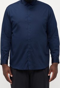 Camicia button-up blu navy con maniche lunghe, colletto puntato e una texture liscia. Presenta un orlo dritto e un design slim fit.