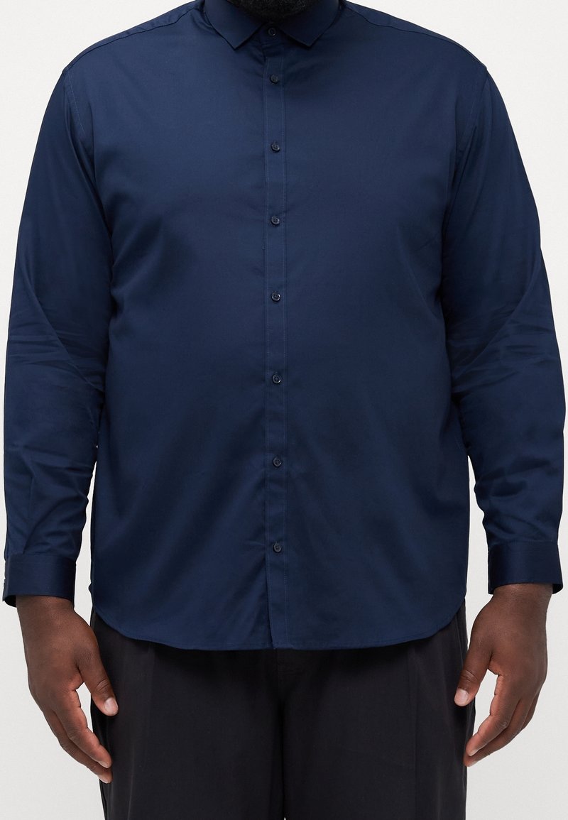 Camicia button-up blu navy con maniche lunghe, colletto puntato e una texture liscia. Presenta un orlo dritto e un design slim fit.