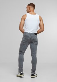 Jeans gris ajustados con una textura suave y un desvanecimiento sutil. Combinados con una camiseta sin mangas blanca y calzado contrastante con acentos negros.